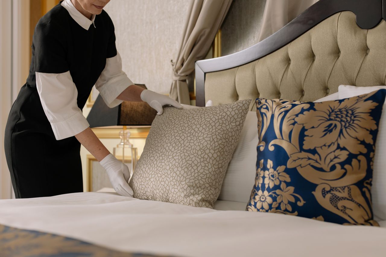 services-03 A chambermaid arranges pillows in a luxurious hotel room, showcasing comfort and elegance.