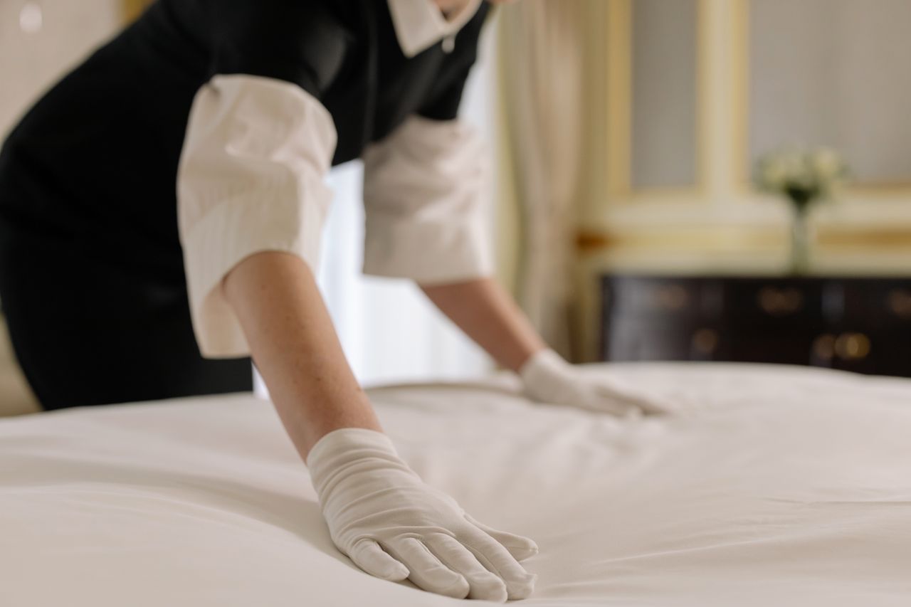 about-img-01 A housekeeper straightening the bed linens in a well-appointed hotel room.