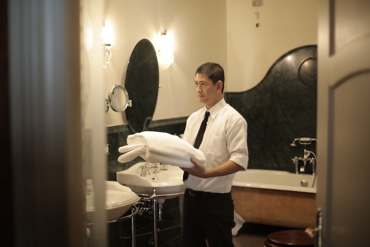 gallery-02 Side view of young male employee holding stack of white towels while standing in bathroom of luxury hotel